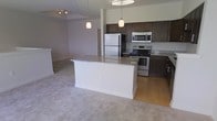This two-floor property at 9410-82 offers a thoughtfully designed open-concept layout that seamlessly connects the kitchen and living areas on the main level. The kitchen is a standout feature, outfitted with dark espresso cabinetry that contrasts elegantly against granite countertops and a full suite of stainless steel appliances, including a refrigerator, electric range, and built-in microwave. A central island with a light granite surface provides additional workspace and serves as a natural dividing point between the kitchen and the adjoining living area. Pendant lighting hangs above the island, complementing the overhead track lighting and contributing to a warm, well-lit atmosphere. The living area transitions smoothly from hardwood-style flooring in the kitchen to plush neutral carpeting, adding comfort underfoot. The open sightlines between rooms enhance the sense of space throughout the main floor. With two levels, the property offers separation between living and private spaces, making it a functional and versatile layout suited to a variety of lifestyles.