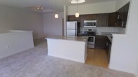 This two-floor property at 9410-82 offers a thoughtfully designed open-concept layout that seamlessly connects the kitchen and living areas on the main level. The kitchen is a standout feature, outfitted with dark espresso cabinetry that contrasts elegantly against granite countertops and a full suite of stainless steel appliances, including a refrigerator, electric range, and built-in microwave. A central island with a light granite surface provides additional workspace and serves as a natural dividing point between the kitchen and the adjoining living area. Pendant lighting hangs above the island, complementing the overhead track lighting and contributing to a warm, well-lit atmosphere. The living area transitions smoothly from hardwood-style flooring in the kitchen to plush neutral carpeting, adding comfort underfoot. The open sightlines between rooms enhance the sense of space throughout the main floor. With two levels, the property offers separation between living and private spaces, making it a functional and versatile layout suited to a variety of lifestyles.