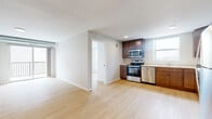 This single-floor residential unit offers a thoughtfully designed open-concept layout that seamlessly connects the living area to the kitchen. Light hardwood flooring runs throughout the space, complementing the neutral-toned walls and white baseboards to create a clean, contemporary aesthetic. The textured ceilings add subtle character to each room.

The kitchen is well-equipped with a full suite of stainless steel appliances, including an electric range, over-the-range microwave, dishwasher, and refrigerator. Rich, dark-toned wood cabinetry provides ample storage, while light countertops offer generous prep space. A window above the sink allows natural light to brighten the workspace.

The open living area benefits from additional natural light through a large window with vertical blinds, creating an airy and welcoming atmosphere. A separate bedroom features floor-to-ceiling windows on two walls, offering expansive views of the surrounding urban landscape and flooding the room with daylight. Additional rooms present versatile, neutral spaces with the same consistent hardwood flooring.

The bathroom includes a full soaking tub with a clean white surround and a brushed nickel grab bar, maintaining the unit's understated, functional design. Overall, the space delivers a modern, move-in-ready environment with consistent finishes throughout.