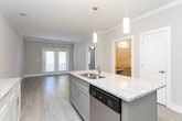 Located at 5402 Freedom Ln in Greensboro, North Carolina, this single-floor residence offers a thoughtfully designed layout with modern finishes and functional living spaces. The kitchen serves as a central highlight, featuring white shaker-style cabinetry extending to the ceiling, granite countertops, stainless steel appliances including a refrigerator, microwave, and range, and a two-tone center island with a built-in sink and pendant lighting above. Light wood-look flooring runs throughout the kitchen and connects seamlessly to the adjacent living areas. The living room is bright and welcoming, showcasing crown molding, neutral walls, and a set of French doors that allow natural light to fill the space. A secondary room with a door leading outside and wood-look flooring offers flexible use. Bedrooms are carpeted and generously sized, with ceiling fans and windows providing natural light and ventilation. A walk-in closet with wire shelving provides ample storage. The bathroom is well-appointed with granite countertops, a gray vanity with dual-tone hardware, a large mirror, tile flooring, and a wall-mounted medicine cabinet. The overall design maintains a clean, contemporary aesthetic with neutral tones throughout.