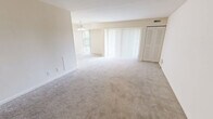 Located at 2118 Haven't Rd in Wilmington, Delaware, this unit presents a practical and comfortable single-floor layout across three bedrooms, one bathroom, a kitchen, and a dedicated laundry space. The living area is notably open and bright, featuring soft neutral-toned walls, wall-to-wall carpeting, and large sliding glass doors dressed with vertical blinds that allow abundant natural light to flow throughout. A chandelier accent adds a touch of character to the dining area adjacent to the main living space. The kitchen is well-appointed with warm wood cabinetry, dark speckled countertops, tile flooring, and a full suite of white appliances including a gas range, dishwasher, refrigerator, and built-in microwave, offering both functionality and storage. The spacious primary bedroom features plush carpeting and a wide bifold closet with built-in shelving and hanging rods, providing ample organization. The additional bedrooms are similarly carpeted and well-proportioned, each with closet access and windows that invite natural light. Clean, neutral finishes are carried consistently throughout the unit, creating a cohesive and move-in-ready atmosphere suited for a range of living arrangements.