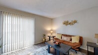 Located at 11500 Green Plaza Dr in Houston, TX, this single-floor unit offers a functional and well-organized layout designed for comfortable everyday living. The living room serves as the central gathering space, featuring durable wood-look flooring, a textured ceiling, and a large sliding glass door dressed with vertical blinds that fills the room with natural light. Adjacent to the living area, the dining room provides a dedicated space for meals, complete with matching wood-look flooring, a window for additional natural light, and a convenient pass-through window connecting directly to the kitchen. The kitchen is equipped with essential appliances, including a refrigerator, dishwasher, and ample countertop and cabinet space. A hallway leads to the private quarters, where the primary bedroom features plush carpet, neutral tones, and a spacious walk-in closet. The secondary bedroom also features carpet flooring and includes built-in shelving and a desk area, making it well-suited as a guest room or home office. A walk-in utility closet provides additional storage. The bathroom is accessible via a private hallway and features a vanity with under-sink storage and a large mirror. Throughout the unit, consistent neutral color palettes and clean finishes contribute to a cohesive, understated aesthetic.