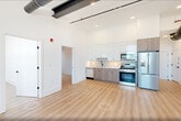 This contemporary apartment, located at 25 E 22nd St in Bayonne, offers 790 square feet of efficiently designed living space. The open-concept floor plan maximizes the use of space, combining the kitchen and living areas for a spacious feel. The kitchen is a standout feature, boasting sleek white upper cabinets contrasted with warm wood lower cabinets, stainless steel appliances, and a stylish geometric backsplash.

Large windows throughout the apartment flood the rooms with natural light and provide views of the surrounding neighborhood. The primary bedroom, measuring 140 square feet, offers ample space for a comfortable retreat. Light-toned wood flooring runs throughout, creating a cohesive and modern aesthetic.

The bathroom features a clean, minimalist design with a wood vanity, large mirror, and modern lighting. Exposed ductwork in some areas adds an industrial touch to the otherwise polished interior. With its blend of style and functionality, this apartment presents an attractive option for those seeking contemporary urban living in Bayonne.