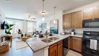 Located at Two Addison Place in Pooler, Georgia, this single-floor residence offers a thoughtfully designed open-concept layout that seamlessly connects the kitchen, dining, and living areas. The kitchen is a standout feature, showcasing rich warm-toned cabinetry, granite countertops, a peninsula island with a double-basin sink and pendant lighting, and a full suite of black appliances including a range, microwave, and refrigerator. Wood-look plank flooring extends throughout the main living areas, adding warmth and visual continuity. The living room is generously proportioned, bathed in natural light through multiple large windows dressed with elegant curtain panels, and features a ceiling fan overhead. The primary bedroom provides a comfortable retreat with plush carpeting, a soothing accent wall, a ceiling fan, natural light from large windows, and direct access to a walk-in closet. The bathroom is well-equipped with granite-topped cabinetry, an undermount sink, a full soaking tub with shower, and an adjacent linen closet with built-in shelving. Throughout the space, clean white walls and consistent finishes contribute to a cohesive, modern aesthetic that is both functional and welcoming.
