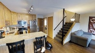 This two-floor residence offers a well-organized layout designed for comfortable everyday living. The main floor centers around an open-concept kitchen equipped with stainless steel appliances, including a refrigerator, double wall oven, and range. Rich natural wood cabinetry provides ample storage, while a granite-topped breakfast bar with seating creates a casual dining space and a natural boundary between the kitchen and the adjoining living area. Hardwood flooring flows throughout the main level, lending warmth and continuity to the space. A textured ceiling with track lighting illuminates the kitchen efficiently. Adjacent to the kitchen, a hallway leads to additional rooms, including what appears to be a laundry area and utility spaces, with warm wood-toned doors adding a consistent design element throughout. A carpeted staircase with a sleek black metal railing provides access to the second floor, adding a modern contrast to the warm wood tones of the main level. The overall ambiance of the space is functional and inviting, with a cohesive blend of natural wood finishes, stone surfaces, and contemporary stainless steel fixtures that together create a practical yet aesthetically considered home environment across both floors.