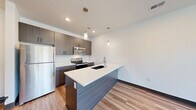 Located at 8310 N Green Hills Rd in Kansas City, MO, this well-designed one-bedroom, one-bathroom unit offers a thoughtful single-floor layout with modern finishes throughout. The open-concept kitchen and dining area serves as the heart of the home, showcasing dark wood cabinetry, crisp white quartz countertops, a peninsula island with an undermount sink, and a full suite of stainless steel appliances including a refrigerator, electric range, microwave, and dishwasher. Stylish pendant lighting adds a contemporary touch above the island. Light-toned wood-style flooring flows through the main living and kitchen areas, complementing the clean, neutral color palette. The living room is bright and airy, featuring a ceiling fan and a large window that invites natural light and outdoor views. The bedroom offers a comfortable and quiet retreat with plush carpeting, a ceiling fan, and a window with exterior views and blinds for privacy. Two closets provide ample storage. The bathroom features a modern vanity with blue cabinetry, white countertops, and wood-style flooring. A dedicated laundry area and utility room add everyday convenience to this efficiently organized and contemporary home.