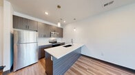 Located at 8310 N Green Hills Rd in Kansas City, MO, this well-designed one-bedroom, one-bathroom unit offers a thoughtful single-floor layout with modern finishes throughout. The open-concept kitchen and dining area serves as the heart of the home, showcasing dark wood cabinetry, crisp white quartz countertops, a peninsula island with an undermount sink, and a full suite of stainless steel appliances including a refrigerator, electric range, microwave, and dishwasher. Stylish pendant lighting adds a contemporary touch above the island. Light-toned wood-style flooring flows through the main living and kitchen areas, complementing the clean, neutral color palette. The living room is bright and airy, featuring a ceiling fan and a large window that invites natural light and outdoor views. The bedroom offers a comfortable and quiet retreat with plush carpeting, a ceiling fan, and a window with exterior views and blinds for privacy. Two closets provide ample storage. The bathroom features a modern vanity with blue cabinetry, white countertops, and wood-style flooring. A dedicated laundry area and utility room add everyday convenience to this efficiently organized and contemporary home.