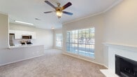 This single-story residence is designed with an open, flowing layout that seamlessly connects the main living areas. The living room is a welcoming focal point, featuring plush neutral carpet, crown molding, a ceiling fan with light kit, and a classic fireplace framed by a clean white mantel. Large windows fitted with horizontal blinds allow generous natural light to fill the space while offering outdoor views, and a glass panel door provides direct exterior access.

The kitchen is thoughtfully integrated into the open floor plan via a peninsula counter with a built-in sink, offering both workspace and a casual dining option. White cabinetry provides ample storage, and stainless steel appliances — including a refrigerator, electric range, and microwave — deliver a modern, functional aesthetic. Light wood-look flooring grounds the kitchen area, contrasting with the carpeted living spaces.

The bedrooms are carpeted and well-lit by natural light through blinds-covered windows. One bedroom features a spacious walk-in closet, offering practical storage. The bathroom is efficiently designed with wood-look tile flooring, a white vanity with cabinetry, a tub and shower combination with tile surround, and open shelving above the vanity for additional storage. Throughout, neutral tones and clean finishes create a cohesive, understated ambiance.