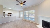 This single-story residence is designed with an open, flowing layout that seamlessly connects the main living areas. The living room is a welcoming focal point, featuring plush neutral carpet, crown molding, a ceiling fan with light kit, and a classic fireplace framed by a clean white mantel. Large windows fitted with horizontal blinds allow generous natural light to fill the space while offering outdoor views, and a glass panel door provides direct exterior access.

The kitchen is thoughtfully integrated into the open floor plan via a peninsula counter with a built-in sink, offering both workspace and a casual dining option. White cabinetry provides ample storage, and stainless steel appliances — including a refrigerator, electric range, and microwave — deliver a modern, functional aesthetic. Light wood-look flooring grounds the kitchen area, contrasting with the carpeted living spaces.

The bedrooms are carpeted and well-lit by natural light through blinds-covered windows. One bedroom features a spacious walk-in closet, offering practical storage. The bathroom is efficiently designed with wood-look tile flooring, a white vanity with cabinetry, a tub and shower combination with tile surround, and open shelving above the vanity for additional storage. Throughout, neutral tones and clean finishes create a cohesive, understated ambiance.