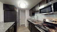 Located at 15420 Livingston Ave in Lutz, Florida, this single-floor residence offers a well-designed layout with a comfortable and functional living environment. The kitchen is a standout feature, showcasing dark espresso cabinetry, granite countertops, a subway tile backsplash, stainless steel appliances including a refrigerator, range, microwave, and dishwasher, alongside a deep double-basin sink with a modern faucet. A peninsula with matching granite provides additional prep and bar-style seating space. The open-concept living and dining areas are finished with durable wood-style flooring and ceiling fans, while large windows with blinds invite natural light and views of the surrounding landscape. A secondary living or flex space also features wood-style flooring and direct access to additional rooms. The bedrooms are carpeted for comfort, each equipped with ceiling fans, natural light from windows, and closet storage. The bathroom is clean and bright, featuring a full tiled tub-shower combo with a safety grab bar. A textured ceiling treatment is consistent throughout the unit, and neutral wall tones create a cohesive, move-in-ready aesthetic throughout the entire space.