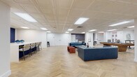 Located at 425 W 5th St in the heart of uptown Charlotte, NC, this single-floor amenity space is designed to offer a dynamic blend of relaxation, collaboration, and entertainment. The entire floor is unified by striking herringbone-patterned light wood flooring, complemented by white coffered ceilings with recessed panel lighting that create a clean, polished atmosphere throughout.

The open main lounge area is generously proportioned, featuring a pair of blue leather sofas, rust-colored velvet ottomans, and a marble-top coffee table, creating an inviting social hub. Adjacent to the lounge is a game area centered on a billiard table, adding a recreational focal point. A bold navy and gold geometric accent wall defines the bar area, which includes a white island with bar seating, blue tile backsplash, and a wall-mounted television. A dedicated workspace with a standing-height table and high stools provides flexible co-working options near windows that bring in natural light.

A private conference room features a solid wood dining-style table, leather chairs, a wall-mounted display, and large windows overlooking greenery. Mailboxes and package lockers are neatly integrated into one entryway corridor, reinforcing the functional design of the space. Throughout, the interiors balance modern elegance with practical amenities.