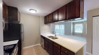 Located at 1256 Johnson Dr in Buffalo Grove, IL, this single-floor residence offers a well-designed layout with practical finishes throughout. The kitchen is a standout feature, equipped with rich dark-stained cabinetry extending to the ceiling for ample storage, light-toned countertops, a double-basin stainless steel sink, and a full suite of stainless steel appliances including a range, over-the-range microwave, dishwasher, and refrigerator. The kitchen flows openly toward the living area, enhanced by vertical blinds that allow natural light to filter through. The living and bedroom spaces feature neutral-toned carpet and warm beige walls, creating a comfortable and inviting ambiance. Large windows with blinds bring in natural light and offer views of the surrounding neighborhood. One room includes direct access to an exterior door, adding convenience. The bathroom is cleanly appointed with a tiled tub and shower combination, a curved chrome curtain rod, a single-sink vanity with dark cabinetry, and a well-lit mirror. Tile flooring in the bathroom and kitchen transitions seamlessly to carpeted areas throughout the rest of the home. The entry foyer provides a welcoming introduction to the space with easy access to the main living areas.
