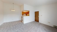 This single-floor 1-bedroom, 1-bathroom unit offers a functional and straightforward layout designed for comfortable everyday living. The living area is generously sized, featuring neutral carpet, a wall-mounted air conditioning unit, and a sliding glass door with vertical blinds that fills the space with natural light and provides outdoor access. A pass-through opening with a breakfast bar connects the living and dining area to the kitchen, giving the layout an open, connected feel. A pendant chandelier adds a subtle decorative touch overhead.

The galley-style kitchen is efficiently organized with warm oak cabinetry lining both sides, offering ample upper and lower storage. Light laminate countertops, a stainless steel sink, a white refrigerator, an electric range, and a dishwasher provide all essential appliances in a compact, easy-to-navigate space.

The bedroom is a comfortable, quiet retreat with plush carpeting, a window with blinds that brings in natural light, and a baseboard heating unit. Neutral walls keep the room bright and versatile.

The full bathroom features classic mosaic tile flooring in a beige and white pattern, a wood vanity with a light countertop, a combination tub and shower with a white surround, grab bars, and a built-in shelf niche. Baseboard heating ensures year-round comfort.
