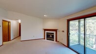 This single-floor residence offers a functional and comfortable layout across several well-defined spaces. The living room serves as the central gathering area, featuring plush wall-to-wall carpeting, a tile-surround fireplace with a warm wood mantel, and a sliding glass door that opens to a balcony overlooking lush greenery, filling the room with natural light and outdoor views.

The kitchen is generously sized with an L-shaped configuration, outfitted with rich oak cabinetry providing ample storage, white laminate countertops, a double stainless steel sink, a dishwasher, an electric range, and a full-size refrigerator. Light tile flooring completes the practical workspace.

The bedroom area benefits from vaulted ceilings, soft carpeting, and a window framing tree views. A spacious walk-in closet serves the space, featuring wrap-around wood shelving and dedicated hanging rods for organized storage.

Two bathrooms are present throughout the unit. Each includes an oak vanity with a white countertop, a framed mirror, and tile-pattern flooring. One bathroom is equipped with accessibility grab bars. Warm wood trim and baseboards appear consistently throughout, contributing to a cohesive and traditional aesthetic across the entire space.