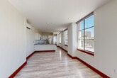 Located at 110 W Ocean Blvd in Long Beach, CA, this 1-bedroom, 1-bathroom unit offers a well-designed layout with a seamless flow between the kitchen and living area. Light hardwood-style flooring and bold red baseboards run throughout, adding a distinctive contrast to the neutral white walls and ceilings.

The open-concept kitchen and living room is a standout feature, with the kitchen showcasing white shaker cabinetry, a white subway tile backsplash, dark quartz countertops, a peninsula with a sink, and stainless steel appliances including a range, over-the-range microwave, and refrigerator. Large floor-to-ceiling windows and glass doors flood the living area with natural light and provide direct access to an outdoor space, with views of the surrounding Long Beach cityscape.

The bedroom is a comfortable size, featuring double sliding closets for ample storage, a wall-mounted split-system air conditioning unit, and continued hardwood-style flooring. The bathroom is finished with a vessel sink atop a white vanity with quartz counters, a large wall mirror, white subway tile accents, and terrazzo-style flooring, contributing to a clean, contemporary aesthetic throughout.