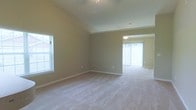 Located at 20 Bur Reed Rd. in Delaware, Ohio, this single-floor home offers a well-designed layout with a focus on open, comfortable living. The interior is defined by soaring vaulted ceilings in the main living area, which lend a sense of spaciousness and airiness to the space. Neutral-toned walls and plush wall-to-wall carpeting create a warm, cohesive aesthetic throughout. Large windows fitted with blinds allow abundant natural light to fill the rooms, enhancing the bright and welcoming ambiance. The living area flows seamlessly into an adjoining room — likely a dining area — which features its own ceiling light fixture and sliding glass doors that invite additional natural light and provide access to the outdoors. The open-concept design between these two areas makes the home feel expansive and well-connected. Clean white trim and baseboards provide a crisp contrast to the soft, earthy wall tones. The single-floor layout ensures convenient, step-free accessibility throughout the entire home, making it both practical and easy to navigate. Overall, the space presents a tidy, move-in ready environment with classic design elements suited for comfortable everyday living.