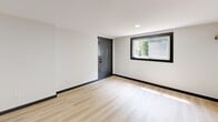 Located at 2436 Belvedere Ave in Knoxville, Tennessee, this thoughtfully designed studio makes efficient use of its single-floor layout. Light-toned luxury vinyl plank flooring runs throughout the space, creating a clean, cohesive aesthetic that is complemented by crisp white walls and bold dark baseboards and door trim.

The open-plan living, dining, and kitchen area forms the heart of the unit. The living space is bright and airy, benefiting from a large window that frames a view of surrounding greenery and allows generous natural light to fill the room. Recessed lighting and a wall-mounted mini-split HVAC unit provide comfortable climate control. A dark-painted closet with double doors offers dedicated storage.

The galley-style kitchen is well-appointed, featuring gray shaker cabinetry with matte black hardware, speckled granite countertops, a stainless steel single-basin sink with a matte black pull-down faucet, a smooth-top electric range, and an overhead microwave — maximizing functionality within a compact footprint.

The bathroom showcases elegant marble-look tile surrounds in the tub/shower combo, accented by matte black fixtures and a built-in niche shelf. The overall design palette — neutral tones, modern finishes, and consistent dark accents — gives the space a polished, contemporary character throughout.