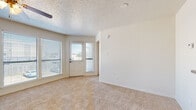 This single-story unit presents a practical and cohesive layout across its main living areas. The living room serves as the central gathering space, featuring plush wall-to-wall carpeting, a ceiling fan with light fixture, and a textured popcorn ceiling. Large windows fitted with horizontal blinds allow abundant natural light to fill the room, while a front entry door with a sidelite panel provides additional brightness and outdoor views. The open, neutral-toned walls create a clean, versatile backdrop throughout.

The galley-style kitchen runs efficiently along two parallel walls, outfitted with warm honey-toned wood cabinetry, dark laminate countertops, and hardwood-style flooring. Stainless steel appliances—including a refrigerator, electric range, microwave, and dishwasher—are integrated seamlessly. A double basin sink sits beneath upper cabinetry, maximizing storage and functionality.

The bedroom mirrors the living area's design with soft carpeting, a ceiling fan, and a window that introduces natural light. The bathroom features hardwood-style flooring, a wood-toned vanity with a white countertop, and a tub-shower combination with classic white subway tile and a decorative wood-tone tile accent border, lending a clean, updated appearance. Overall, the unit maintains a neutral, functional aesthetic throughout.