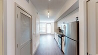 This single-floor unit presents a clean, modern aesthetic throughout, with wood-style flooring and a neutral color palette creating a cohesive and inviting atmosphere. The kitchen is efficiently designed along one wall, featuring white cabinetry with black hardware, a dark tile backsplash, light countertops, and a full suite of stainless steel appliances including a refrigerator, gas range, microwave, and dishwasher. Pendant lighting illuminates the corridor leading toward the main living area.

The living space is generously proportioned, receiving abundant natural light through large windows and a glass door that opens to the exterior. A ceiling fan adds both function and a finishing touch to the room. The same wood-style flooring continues throughout, maintaining visual consistency.

The bedroom is spacious and bright, featuring a ceiling fan, warm-toned hardwood-style floors, and direct access to a walk-in closet with built-in shelving — offering practical and organized storage.

The bathroom is finished with light tile flooring, warm wood-toned cabinetry, a wide white countertop with an undermount sink, a large framed mirror with overhead lighting, wall-mounted storage, and a tiled shower, combining style with functionality throughout.