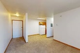 This single-floor, one-bedroom, one-bathroom unit offers a practical and efficient layout across a compact footprint. The open living area is finished with neutral-toned carpet and white walls, creating a clean, bright atmosphere. A large window fitted with vertical blinds allows natural light to fill the space, while a wall-mounted air conditioning unit and baseboard heating provide year-round climate control.

The kitchen is separated from the living area and features warm-toned wood cabinetry, a white refrigerator, a sink, and durable tile flooring, providing a functional space for meal preparation. The layout allows for easy flow between the kitchen and main living space via a connecting hallway, which also leads to the entry door.

The bedroom is a well-proportioned, carpeted room equipped with a ceiling fan, a window with blinds for natural light and privacy, baseboard heating, and a sliding double-door closet offering practical storage. The full bathroom includes a tiled shower-tub combination with yellow accent tile, a toilet, and a vanity with cabinet storage, all set on classic mosaic tile flooring. Overall, the unit presents a straightforward, functional design suited for efficient single-occupant living.