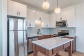Located at 826 Williamson St in Madison, Wisconsin's vibrant Williamson Street corridor, this thoughtfully designed one-bedroom, one-bathroom unit makes excellent use of its compact footprint. Light hardwood flooring flows consistently throughout, lending warmth and visual continuity to the entire space.

The kitchen serves as the centerpiece of the unit, featuring a two-tone cabinetry design with white upper cabinets and warm wood-toned lower cabinets, complemented by a classic subway tile backsplash. Stainless steel appliances — including a full-size refrigerator, range, microwave, and dishwasher — provide a modern, functional finish. A freestanding wood kitchen island with a white countertop and built-in storage adds both workspace and character. Globe pendant lights overhead contribute a warm, inviting ambiance.

The bedroom is a clean, bright space with white walls, a ceiling fan, and a sliding door that opens directly to a dedicated closet with built-in shelving — a practical and space-saving design choice.

The bathroom maintains the unit's modern aesthetic with warm wood cabinetry, a white quartz countertop, matte black fixtures and hardware, and light wood-style flooring. A hallway with recessed lighting connects the rooms efficiently, completing the unit's well-organized and contemporary layout.