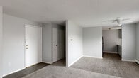 Located at 104 Grecian Gardens Dr in Rochester, NY, this single-floor, one-bedroom unit offers a straightforward and efficient layout. The living room is the largest shared space, featuring neutral gray walls, a textured ceiling, and a combination of soft carpet and wood-look vinyl flooring. Two windows along one wall allow natural light to fill the room, and a wall-mounted air conditioning unit provides climate control. Baseboard heating runs along the perimeter, consistent throughout the unit.

The kitchen is a galley-style space with dark hardwood-style flooring, gray lower cabinetry, and white upper cabinets. A mosaic tile backsplash accents the cooking area, which includes a black refrigerator, a gas range, and a stainless steel sink beneath a window. Light stone-patterned countertops provide ample prep space along both sides of the kitchen.

The bedroom is a well-proportioned private retreat with plush carpeting, a window with a blind for light control, baseboard heating, and a set of bifold closet doors offering generous storage. Two hallways connect the rooms, providing defined circulation throughout the unit. The overall aesthetic is clean and neutral, with a consistent gray palette across all spaces.