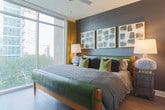Located in the heart of Midtown Atlanta, this well-appointed single-floor residence offers a thoughtfully designed layout that balances contemporary style with functional living. The open-concept kitchen is a standout feature, showcasing gray shaker cabinetry, stainless steel appliances, white quartz countertops, subway tile backsplash, and a large island with bar seating — all illuminated by pendant lighting and recessed fixtures. Wide-plank hardwood-style flooring flows throughout the space, tying each room together cohesively. The living area is defined by dramatic floor-to-ceiling sliding glass doors that open to a private balcony, filling the room with natural light and offering sweeping views of the Atlanta skyline. The primary bedroom features large windows with city views, a bold accent wall, and access to a well-appointed bathroom with gray cabinetry and a walk-in closet outfitted with custom built-in shelving and drawers. Additional bedrooms continue the design language with accent walls, generous natural light, and modern finishes. Throughout the residence, curated artwork and bold color choices contribute to a sophisticated, urban aesthetic that reflects the energy of its Midtown Atlanta surroundings.