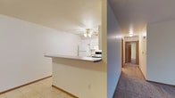This single-floor residential unit offers a practical and functional layout designed for comfortable everyday living. The kitchen is outfitted with white cabinetry, a white refrigerator, and an electric range, all complemented by a ceiling fan with an integrated light fixture that keeps the space bright and well-ventilated. A peninsula-style breakfast bar extends from the kitchen wall, creating a convenient pass-through that connects the kitchen to the adjacent living or dining area, promoting an open and sociable atmosphere. The kitchen flooring features light-toned tile, providing a clean and easy-to-maintain surface. From the main living area, a carpeted hallway extends toward the private areas of the unit, including what appears to be one or more bedrooms with wood-paneled doors. The warm-toned carpet in the hallway and adjoining rooms adds a layer of comfort underfoot. The walls throughout are finished in a neutral off-white palette, creating a bright and cohesive aesthetic that offers a versatile backdrop for a variety of interior styles. Overall, the space presents a straightforward, well-organized floor plan suited for efficient single-floor living.