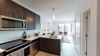 This thoughtfully designed single-floor residence offers a seamless blend of modern style and functional living. The open-concept layout connects the kitchen directly to the living area, creating an airy, cohesive space ideal for everyday living and entertaining. The kitchen is outfitted with rich dark-espresso cabinetry, a white tile backsplash, light quartz countertops, and a full suite of stainless steel appliances including a refrigerator, range, microwave, and dishwasher. Light wood-tone flooring runs throughout the main living areas, adding warmth and continuity. The living room is bright and welcoming, anchored by a floor-to-ceiling sliding glass door that floods the space with natural light and opens to an outdoor view of the surrounding building. The bedroom is a calm retreat, finished with soft carpeting, neutral-toned walls, and ample space for a full furniture arrangement. The bathroom features a walk-in shower with a curved curtain rod, a dark-cabineted vanity with a white countertop, a single undermount sink, and wood-look tile flooring. Clean white walls and contemporary fixtures throughout the residence contribute to a cohesive, modern aesthetic that is both practical and visually inviting.