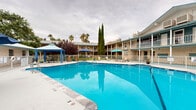 Located at 6770 Edgemere Blvd in El Paso, Texas, this outdoor amenity space centers around a generously sized swimming pool with vivid blue water, offering a welcoming retreat in the heart of the Borderland sun. The pool area is fenced for safety and framed by a well-maintained concrete deck outfitted with lounge chairs, patio tables, and umbrellas — providing ample space for both relaxation and socializing.

A standout feature is the blue-accented gazebo positioned poolside, offering a shaded gathering spot complete with seating. Multiple umbrella stations are distributed around the deck, ensuring additional shade throughout the day. The surrounding landscape includes mature palm trees, tall cypress trees, and ornamental shrubs that lend the space a lush, resort-like character.

The pool area is enclosed by a multi-story building featuring covered balconies and exterior corridors, giving the courtyard a sense of enclosure and privacy. The brick and stucco facade, accented with teal and blue trim, contributes a classic Southwestern architectural character to the overall aesthetic. A low-profile clubhouse or amenity building is visible poolside, providing additional functional support to the outdoor space. The entire area conveys a clean, well-kept, and inviting atmosphere suitable for leisure and recreation.