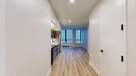This 340 square foot studio apartment in New York City offers a thoughtfully designed living space. The open-concept layout maximizes the available area, creating a sense of spaciousness despite its compact size. The apartment features light wood flooring throughout, enhancing the bright and airy atmosphere.

The modern kitchen is a standout element, boasting stainless steel appliances, including a refrigerator, microwave, and oven. Dark wood cabinetry provides a striking contrast to the white subway tile backsplash and countertops. The kitchen's efficient design allows for ample storage and workspace.

Large windows in the living area flood the space with natural light and offer city views. The room is versatile, easily accommodating both living and sleeping arrangements. Recessed lighting adds to the contemporary feel of the space.

The bathroom is sleek and stylish, featuring a modern vanity with wood cabinetry, a white countertop, and a circular mirror. Beige tile walls and black hardware accents create a sophisticated look. The space includes a toilet and necessary amenities.

This well-appointed studio apartment combines functionality and style, making efficient use of its 340 square feet to provide a comfortable urban living experience in the heart of New York City.