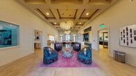 This expansive single-floor clubhouse is a masterclass in eclectic, contemporary design. The main lounge immediately captures attention with soaring coffered ceilings adorned with warm wood accents, oversized woven globe pendant lights, and a seating arrangement of sculptural lattice-back chairs surrounding a colorful floral ottoman atop a vibrant pink area rug. Tall windows and glass doors flood the space with natural light, enhancing the open, airy atmosphere.

Adjacent areas include a sleek bar and game lounge, featuring a tray ceiling, stone-clad accent wall, wall-mounted TV, and a pedestal bistro table with counter-height seating. A stunning full kitchen boasts teal cabinetry, a large white island with bar seating, a beverage refrigerator, and an eye-catching floor-to-ceiling hand-painted mural in vivid tropical hues, illuminated by gold leaf-shaped pendant lights.

Two distinct private meeting or dining rooms offer intimate settings, each furnished with unique tables, eclectic chairs, statement pendant lighting, and large windows. A relaxed lounge area features rich tan leather sofas, a patterned blue rug, and a decorative fireplace surround finished in geometric teal tile. Original artwork is displayed thoughtfully throughout, contributing to a cohesive, gallery-like ambiance across the entire space.