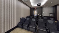 This dedicated private screening room is thoughtfully designed to deliver an immersive cinematic experience. The space is anchored by a large, framed projection screen mounted on a deep charcoal accent wall, flanked by sleek, elongated wall sconces that cast a warm, dramatic glow. A ceiling-mounted projector ensures a high-quality viewing experience for all guests.

Multiple rows of plush, black leather theater-style recliners with integrated cup holders are arranged to provide excellent sightlines from every seat, comfortably accommodating a sizeable group. The seating area is grounded by a neutral, textured carpet that contrasts elegantly with the dark base molding and walls.

The side walls feature a refined, tone-on-tone patterned wallcovering that adds subtle texture and contributes to the room's acoustic quality. A triptych of framed artwork adorns one wall, adding a curated, gallery-like touch to the space.

Toward the rear of the room, a built-in refreshment station with dark wood cabinetry, a stone countertop, and a dedicated popcorn machine elevates the experience with a classic concession touch. Recessed ceiling lighting and strategically placed sconces complete the polished, upscale ambiance of this well-appointed screening room.