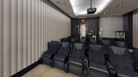 This dedicated private screening room is thoughtfully designed to deliver an immersive cinematic experience. The space is anchored by a large, framed projection screen mounted on a deep charcoal accent wall, flanked by sleek, elongated wall sconces that cast a warm, dramatic glow. A ceiling-mounted projector ensures a high-quality viewing experience for all guests.

Multiple rows of plush, black leather theater-style recliners with integrated cup holders are arranged to provide excellent sightlines from every seat, comfortably accommodating a sizeable group. The seating area is grounded by a neutral, textured carpet that contrasts elegantly with the dark base molding and walls.

The side walls feature a refined, tone-on-tone patterned wallcovering that adds subtle texture and contributes to the room's acoustic quality. A triptych of framed artwork adorns one wall, adding a curated, gallery-like touch to the space.

Toward the rear of the room, a built-in refreshment station with dark wood cabinetry, a stone countertop, and a dedicated popcorn machine elevates the experience with a classic concession touch. Recessed ceiling lighting and strategically placed sconces complete the polished, upscale ambiance of this well-appointed screening room.