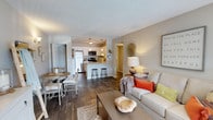 This single-story residence offers a well-designed open-concept layout that seamlessly connects the main living areas. The living room serves as the heart of the home, featuring dark hardwood-style flooring, a textured ceiling, and a large window with vertical blinds that draws in natural light. The space accommodates comfortable seating and a coffee table, creating an inviting atmosphere.

The kitchen is thoughtfully appointed with white shaker-style cabinetry, granite-look countertops, and a full suite of stainless steel appliances, including a refrigerator, range, microwave, and dishwasher. A peninsula with bar seating and pendant lighting overhead connects the kitchen to the dining area, making it ideal for casual meals or entertaining. A separate dining nook provides additional space for a table and chairs.

The bedroom is generously proportioned, featuring plush carpet, a large window for natural light, and access to a walk-in closet. The bathroom continues the cohesive design with a wide granite-top vanity, ample cabinetry, and bright overhead lighting. Neutral tones carry throughout the residence, creating a calm and cohesive ambiance.