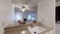 This single-floor residence offers a practical and functional layout connecting the kitchen and living areas in an open, flowing arrangement. The kitchen is equipped with white cabinetry, a electric range, granite-style countertops, a single-basin sink, and tile flooring. A pass-through counter connects the kitchen to the living space, making the area feel cohesive and open. Conveniently, in-unit laundry is accessible directly from the kitchen.

The spacious living room features neutral carpet, textured ceilings, and baseboard heating units along the walls. A ceiling fan with light fixture provides overhead circulation, while a marble-surround fireplace serves as a notable focal point. Vertical blinds on multiple windows allow natural light to fill the room. A wall-mounted air conditioning unit provides additional climate control.

Multiple carpeted bedrooms each feature natural light from windows dressed with vertical blinds and baseboard heating. Closets with built-in shelving provide organized storage in the bedrooms. The bathroom includes a clean, white tub and shower surround. Throughout the residence, a consistent neutral color palette and textured ceilings create a cohesive, understated aesthetic suited for comfortable everyday living.