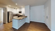 Located at 912 3rd Avenue in Chula Vista, California, this single-floor residence offers a clean, modern aesthetic throughout its well-designed layout. The open-concept living and kitchen area serves as the heart of the home, anchored by a peninsula-style kitchen island with dark countertops and an undermount sink. White shaker-style cabinetry lines the kitchen walls, complemented by stainless steel appliances including a refrigerator, electric range, and over-the-range microwave. Rich wood-style flooring flows seamlessly through the main living areas, adding warmth to the contemporary design. Recessed and track lighting throughout provides excellent illumination. A built-in shelving and cabinetry nook conveniently connects the kitchen to the living space, offering additional storage. The living area is bright and open, with windows dressed in horizontal blinds allowing natural light to filter in. The bedroom features soft carpeting, generous closet space with dedicated walk-in and reach-in options, and a private exterior access door. The bathroom is finished with a full tub-shower combination, a wide vanity with dark countertops, white cabinetry, and a large mirror. A dedicated laundry area is also accessible within the unit. The overall design is cohesive, neutral, and move-in ready.