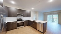 Located at 9800 Diffley Ct in Inver Grove Heights, MN, this well-appointed two-bedroom, two-bathroom residence offers a thoughtfully designed single-floor layout. The open-concept kitchen and living area serves as the heart of the home, featuring rich dark-toned cabinetry, stainless steel appliances including a refrigerator, range, microwave, and dishwasher, along with crisp white countertops and light hardwood-style flooring. A large peninsula provides additional prep space and casual seating. The living room extends naturally from the kitchen and is bathed in natural light through sliding glass doors that open to a private balcony with outdoor views. Both bedrooms are carpeted for comfort, with the primary bedroom featuring a ceiling fan, a bright window, and access to a dedicated bathroom complete with a dark wood vanity, white countertop, and walk-in closet with wire shelving. The second bathroom includes a full soaking tub and shower combination with brushed nickel fixtures. A dedicated laundry room houses a full-size Whirlpool washer and dryer with overhead wire shelving. Neutral tones and consistent finishes throughout the space create a clean, cohesive aesthetic ideal for modern living.