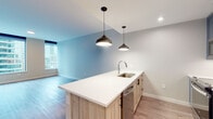 Located in the heart of Midtown Atlanta at 903 Peachtree St NE, this modern single-floor residence offers a thoughtfully designed open-concept layout with contemporary finishes throughout. The living and kitchen areas flow seamlessly together, anchored by a large kitchen island with a crisp white countertop, an undermount stainless steel sink, and stylish pendant lighting. Light wood-toned cabinetry pairs with slate-blue upper cabinets and a full suite of stainless steel appliances, including a refrigerator, range, built-in microwave, and dishwasher. Wide-plank wood-style flooring extends throughout the main living areas, complementing the soft, neutral color palette. Floor-to-ceiling windows invite abundant natural light and offer impressive views of the Atlanta skyline, giving the space an elevated, airy feel. The bedroom is generously proportioned with its own city-facing window. A dedicated in-unit laundry closet with a stacked washer and dryer adds everyday convenience. The bathroom features large-format tile flooring, a light wood vanity, and a glass-enclosed walk-in shower with classic white subway tile. Clean lines, modern hardware, and a bright, open atmosphere define this well-appointed Midtown residence.