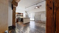 Located at 110 S 15th St in Richmond, VA, this 2-bedroom, 2-bathroom loft-style unit masterfully blends historic industrial character with modern updates. Rich, reclaimed hardwood floors run throughout, complemented by exposed original brick walls and massive hand-hewn timber columns that serve as striking architectural focal points in nearly every room. Ceiling fans with track lighting add both function and an industrial edge to the open, airy layout.

The open-plan living, dining, and kitchen area forms the heart of the unit, where large windows invite natural light and views of the surroundings. The kitchen is well-appointed with dark espresso cabinetry, granite countertops, stainless steel appliances, and a central island with pendant lighting overhead — ideal for both cooking and entertaining.

Each bedroom continues the loft aesthetic, featuring the same reclaimed hardwood flooring, exposed timber columns, and ceiling fans. The primary bedroom includes two closets for generous storage. Both bathrooms are clean and modern, featuring dark-stained floating vanities with granite countertops, tiled flooring, and tub/shower combinations. A dedicated laundry area and utility room add everyday convenience to this characterful urban retreat.