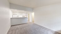This single-floor residence presents a clean, cohesive design highlighted by a bright, neutral palette throughout. The open-concept layout connects the living area to the kitchen, which is outfitted with white shaker-style cabinetry, a subway tile backsplash, a stone-look countertop peninsula, and a full suite of white appliances including a refrigerator, electric range, built-in microwave, and dishwasher. Recessed lighting illuminates the kitchen, while the peninsula provides a natural division between the cooking and living spaces.

The living area features plush grey carpet underfoot, extending into the bedrooms. Each bedroom is generously sized, with large windows dressed in vertical blinds that allow ample natural light. One bedroom includes a ceiling fan, and a closet is accessible from the bedroom corridor.

The bathroom is well-appointed with a white vanity, stone-look countertop, light wood-look flooring, and a tiled tub-shower surround with subway tile detailing. A dedicated laundry room houses a full-size washer and dryer alongside utility shelving. Light wood-look plank flooring carries through the kitchen, entry, bathroom, and laundry areas, tying the space together cohesively.