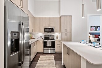 Kitchen with oak cabinetry, undercabinet lighting, white quartz countertops, stainless steel appliances, and hard-surface vinyl plank flooring - Avalon Fort Lauderdale