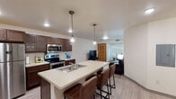 Located at 1004 Vine St in La Crosse, Wisconsin, this single-floor unit offers a well-designed, modern living space with a cohesive layout and contemporary finishes. The open-concept kitchen and living area serve as the heart of the unit, anchored by a spacious island with a built-in sink and seating for multiple bar stools. Rich dark wood cabinetry lines the kitchen walls, complemented by stainless steel appliances including a refrigerator, range, and microwave. Industrial-style pendant lights hang above the island, adding a stylish touch. Light wood-look flooring flows consistently throughout the entire unit, creating a clean and unified aesthetic. The living area offers comfortable seating and flows naturally from the kitchen, with natural light filtering in through window blinds. Multiple bedrooms are present, each featuring ceiling fans, windows with blinds, and ample space for sleeping and study areas. One bedroom includes a dedicated desk workspace. The bathroom features light flooring, a shower with a curtain, and clean, neutral finishes. An additional sitting area provides extra flexible living space. Recessed lighting throughout keeps each room bright and well-illuminated, contributing to the overall modern and functional character of this La Crosse residence.