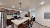 Located at 1004 Vine St in La Crosse, Wisconsin, this single-floor unit offers a well-designed, modern living space with a cohesive layout and contemporary finishes. The open-concept kitchen and living area serve as the heart of the unit, anchored by a spacious island with a built-in sink and seating for multiple bar stools. Rich dark wood cabinetry lines the kitchen walls, complemented by stainless steel appliances including a refrigerator, range, and microwave. Industrial-style pendant lights hang above the island, adding a stylish touch. Light wood-look flooring flows consistently throughout the entire unit, creating a clean and unified aesthetic. The living area offers comfortable seating and flows naturally from the kitchen, with natural light filtering in through window blinds. Multiple bedrooms are present, each featuring ceiling fans, windows with blinds, and ample space for sleeping and study areas. One bedroom includes a dedicated desk workspace. The bathroom features light flooring, a shower with a curtain, and clean, neutral finishes. An additional sitting area provides extra flexible living space. Recessed lighting throughout keeps each room bright and well-illuminated, contributing to the overall modern and functional character of this La Crosse residence.
