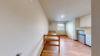 Located on the fourth floor at 4730 20th Ave NE in Seattle's University District, this efficient one-bedroom, one-bathroom unit offers a well-organized layout designed to maximize every square foot. Light wood flooring runs throughout the main living area, lending warmth to the neutral gray and white color palette that defines the space.

The open living and sleeping area is flooded with natural light from a window that frames views of the surrounding neighborhood greenery. The kitchenette is neatly tucked along one wall, featuring white shaker-style cabinetry, a compact stainless steel refrigerator, a built-in microwave, and a single-basin sink — providing all the essential cooking and storage amenities in a streamlined footprint.

The bedroom area is straightforward and functional, with clean walls, light wood flooring, a wall-mounted HVAC vent, and ample room for a standard bed and additional furnishings. The private bathroom is finished with a white vanity with under-sink storage, a toilet, and accessibility-friendly grab bars along the walls. Light tile flooring and a medicine cabinet complete the practical, no-frills design.

Overall, this unit delivers a clean, move-in-ready environment with a sensible layout, making it a practical choice for individuals seeking a no-fuss living space in Seattle's vibrant University District.
