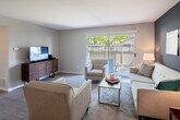 Located at 1630 Orchard Dr in Placentia, California, this single-floor residence offers a thoughtfully designed layout with a cohesive modern aesthetic throughout. The living room serves as the heart of the home, highlighted by a bold teal accent wall, warm hardwood-style flooring, and a sliding glass door that opens to a private outdoor patio, filling the room with natural light and views of surrounding greenery. The space comfortably accommodates a full seating arrangement, anchored by a media console along one wall.

Adjacent to the living area, the dining space features wood-toned flooring, a louvered closet door, and a decorative wall mirror that adds depth to the room. The kitchen is well-appointed with crisp white cabinetry, light quartz countertops, stainless steel appliances including a refrigerator, range, microwave, and dishwasher, and a tray ceiling with recessed lighting that adds architectural interest.

The bedrooms offer a calm, restful atmosphere with plush carpeting, neutral tones, and ample natural light from well-positioned windows with blinds. Both bathrooms are cleanly finished, featuring white vanities, light flooring, and a functional, uncluttered design. Overall, the residence presents a polished, move-in-ready interior with contemporary finishes throughout.