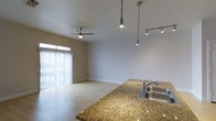 This single-floor Dallas property offers an open-concept layout that seamlessly connects the kitchen and living areas. The kitchen is anchored by a warm-toned granite countertop with a double stainless steel sink, providing both functionality and visual appeal. Pendant and track lighting hang above, offering adjustable illumination that highlights the kitchen's surfaces while extending into the main living space.

The living area benefits from light-toned hardwood-style flooring that runs throughout, creating a cohesive and clean aesthetic. A ceiling fan centered in the room provides both comfort and ambient lighting. Natural light flows generously into the space through a large sliding glass door dressed with vertical blinds, brightening the interior and creating a welcoming atmosphere.

The neutral gray-toned walls and white ceilings keep the space feeling airy and versatile, allowing for a variety of interior design preferences. The combination of thoughtful lighting fixtures, quality surfaces, and an open floor plan makes this Dallas property a functional and attractive single-level living space.