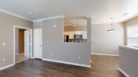 This single-floor residence offers a thoughtfully designed open-concept layout that promotes a seamless flow between the living, dining, and kitchen areas. Rich, dark hardwood-style flooring runs throughout the space, providing a warm and cohesive foundation that complements the neutral warm-gray wall tones and crisp white trim and crown molding.

The kitchen is a functional centerpiece, featuring white cabinetry, granite countertops, and a suite of stainless steel appliances including a range, microwave, refrigerator, and dishwasher. A decorative tile backsplash with a mosaic pattern adds visual interest, while track lighting illuminates the workspace effectively. A half-wall with a granite-topped breakfast bar connects the kitchen to the main living area, creating an open pass-through that enhances the sense of space.

The living and dining areas are bright and airy, benefiting from multiple windows dressed with blinds that allow natural light to filter in. Crown molding and decorative columns add architectural character to the open floor plan.

The bathroom is well-appointed with a granite-top vanity with an undermount sink, white cabinetry, a full tub-shower combination with tiled surround, and brushed nickel fixtures and hardware throughout, maintaining a clean and polished aesthetic.