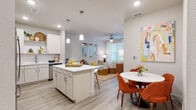 Located on Park Lane in Davenport, Florida, this single-story unit offers a thoughtfully designed open-concept layout that seamlessly connects the kitchen, dining, and living areas. Light wood-tone flooring runs throughout, complementing the neutral color palette and creating a bright, cohesive atmosphere.

The kitchen is a standout feature, equipped with stainless steel appliances, white shaker-style cabinetry, a subway tile backsplash, and a central island with pendant lighting and bar seating. Ample counter space and open shelving add both functionality and visual interest.

The dining area sits adjacent to the kitchen, while the living room benefits from a ceiling fan and natural light from large windows with blinds. Bedrooms are well-proportioned, featuring multiple windows dressed in sheer curtains that invite natural light. A spacious walk-in closet with wire shelving systems provides generous storage. The bathroom includes a wide vanity with quartz-style countertops and a tub-shower combination with tile surround. A dedicated laundry area accommodates a stacked washer and dryer alongside a water heater, rounding out this well-appointed space.