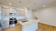 Located in Summerville, SC, this well-appointed 2-bedroom, 1-bathroom home offers a thoughtfully designed single-level layout with modern finishes throughout. The open-concept kitchen and living area serves as the heart of the home, anchored by a generous granite-topped island with an undermount sink and polished pendant lighting. Gray shaker-style cabinetry, a herringbone tile backsplash, stainless steel appliances, and light hardwood flooring complete the kitchen's contemporary aesthetic. The living room is bright and airy, featuring a ceiling fan, recessed lighting, and French doors with a transom window that invite natural light and provide outdoor access. The primary bedroom offers a comfortable footprint with plush carpeting, a ceiling fan, and a walk-in closet outfitted with wire shelving for organized storage. The second bedroom is equally well-lit, with carpeted flooring and a ceiling fan. The bathroom features a frameless glass sliding-door shower with white tile surround, complemented by warm-toned cabinetry. A dedicated laundry room with full-size washer and dryer hookups adds everyday convenience. Clean white walls, consistent trim work, and light wood flooring throughout lend the home a cohesive, move-in-ready appeal.
